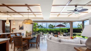 Un interior moderno con comedor, sofá y vistas a un jardín tropical.