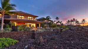 Una casa moderna con piscina, rodeada de un paisaje rocoso y palmeras.