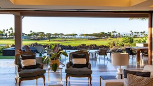 Amplio espacio interior con vista a un campo de golf. Varias sillas y mesas dispuestas para comer o relajarse.