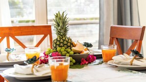 En frukostuppdukning med ananas, melon och glas med juice på ett bord med utsikt över grönskan utanför.