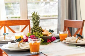 A breakfast setting with a pineapple, melon, and juice glasses on a table with a view of greenery outside. - Romantic villa with private pool and magnificent ocean view (Cas Abao)