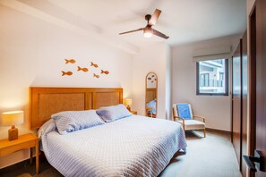 Ein Hotelzimmer mit Bett, Stuhl, Deckenventilator, Fenster und Wanddekorationen.