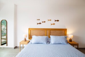 A hotel room with a bed, two bedside tables, a mirror, and wall-mounted fish decorations.