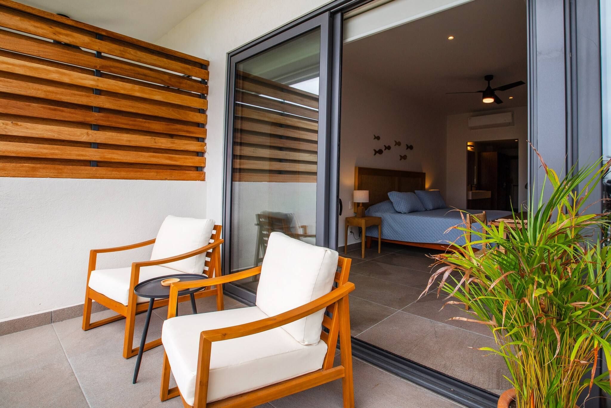 A modern outdoor seating area with wooden chairs and a glass door leading to a bedroom.