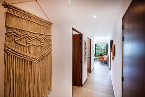 Un pasillo con un tapiz de macramé, puertas de madera y vistas a una sala de estar con una mesa y sillas.
