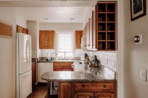A kitchen with wooden cabinets, a white refrigerator, a countertop with a sink, and a window with blinds.