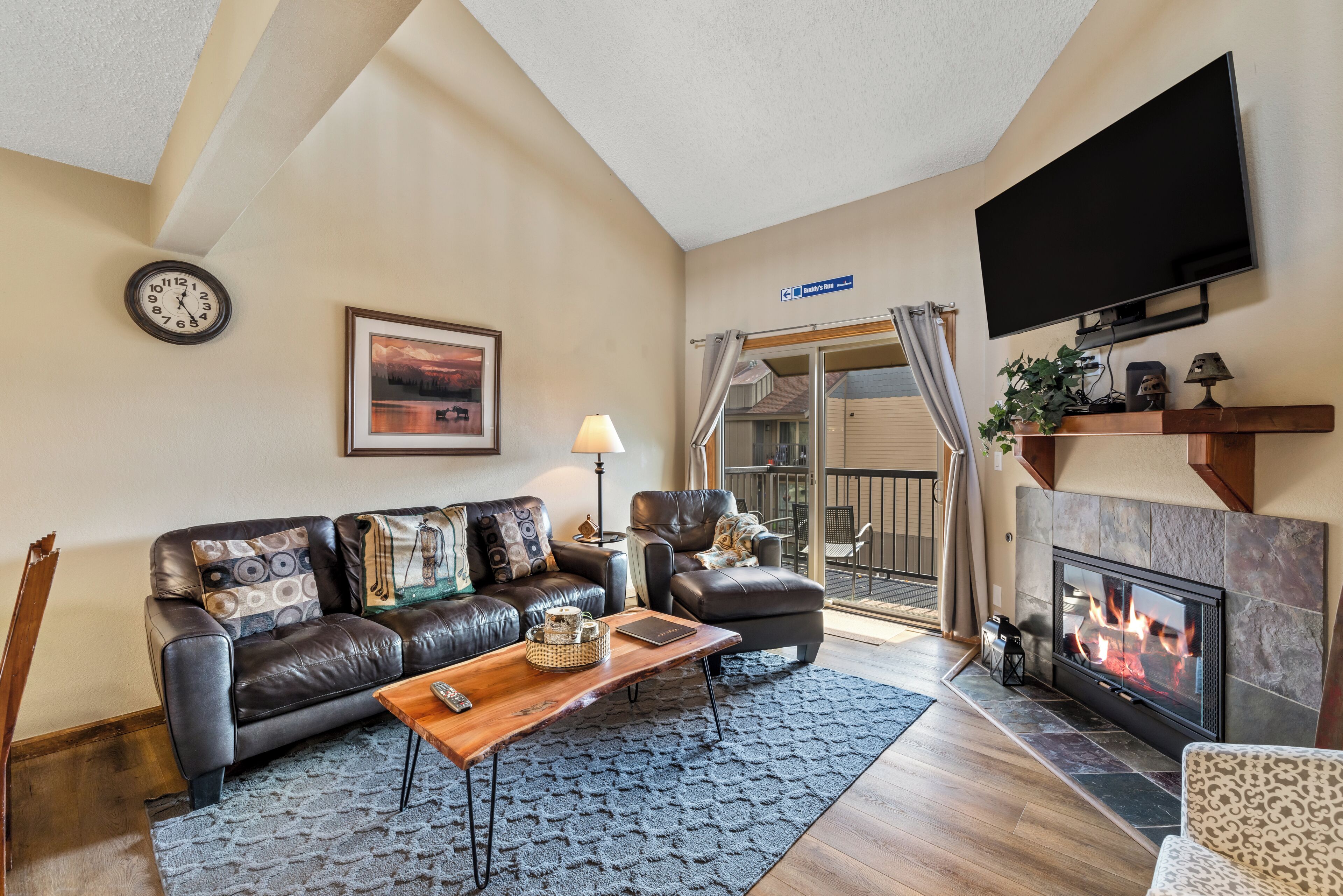 A living room with a leather sofa, a coffee table, a fireplace, a television, and a clock on the wall.