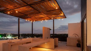 An outdoor terrace with a wooden pergola, string lights, and a city view at dusk. - Private Downtown Studio w/Rooftop Pool (Tulum)