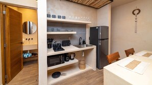 A compact kitchen with a refrigerator, microwave, and sink. There are shelves with cups and plates, and a dining table with chairs. - Private Downtown Studio w/Rooftop Pool (Tulum)