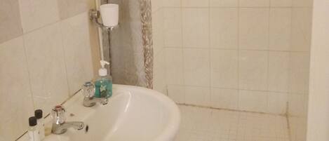 Un baño con un lavabo blanco, un espejo, una ducha con puerta de vidrio y suelo de baldosas.