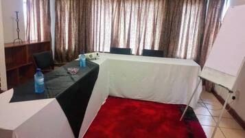 A conference room with a white table, black table runner, and red carpet. There are two chairs, a whiteboard, and a water bottle on the table.