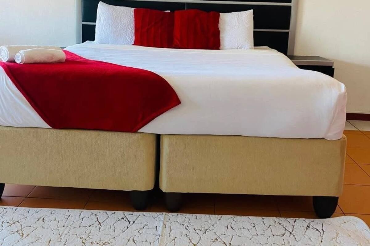 Een net opgemaakt bed met wit en rood beddengoed, een rode plaid en een wit kussen.