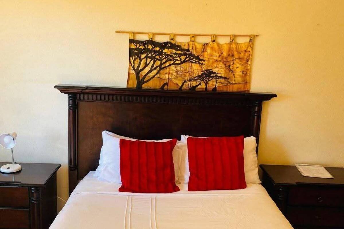 Een netjes opgemaakt bed met wit en rode beddengoed, een houten hoofdbord en een wandtapijt.