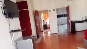 Een hotelgang met een televisie aan de muur, een koelkast en een kitchenette met een spoelbak en aanrecht.