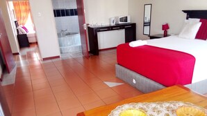 Habitación de hotel con cama, escritorio, microondas, lavamanos y ducha.