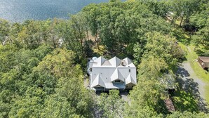 Vista aérea de una casa rodeada de un bosque denso, con una clara vista del paisaje circundante y una masa de agua al fondo.