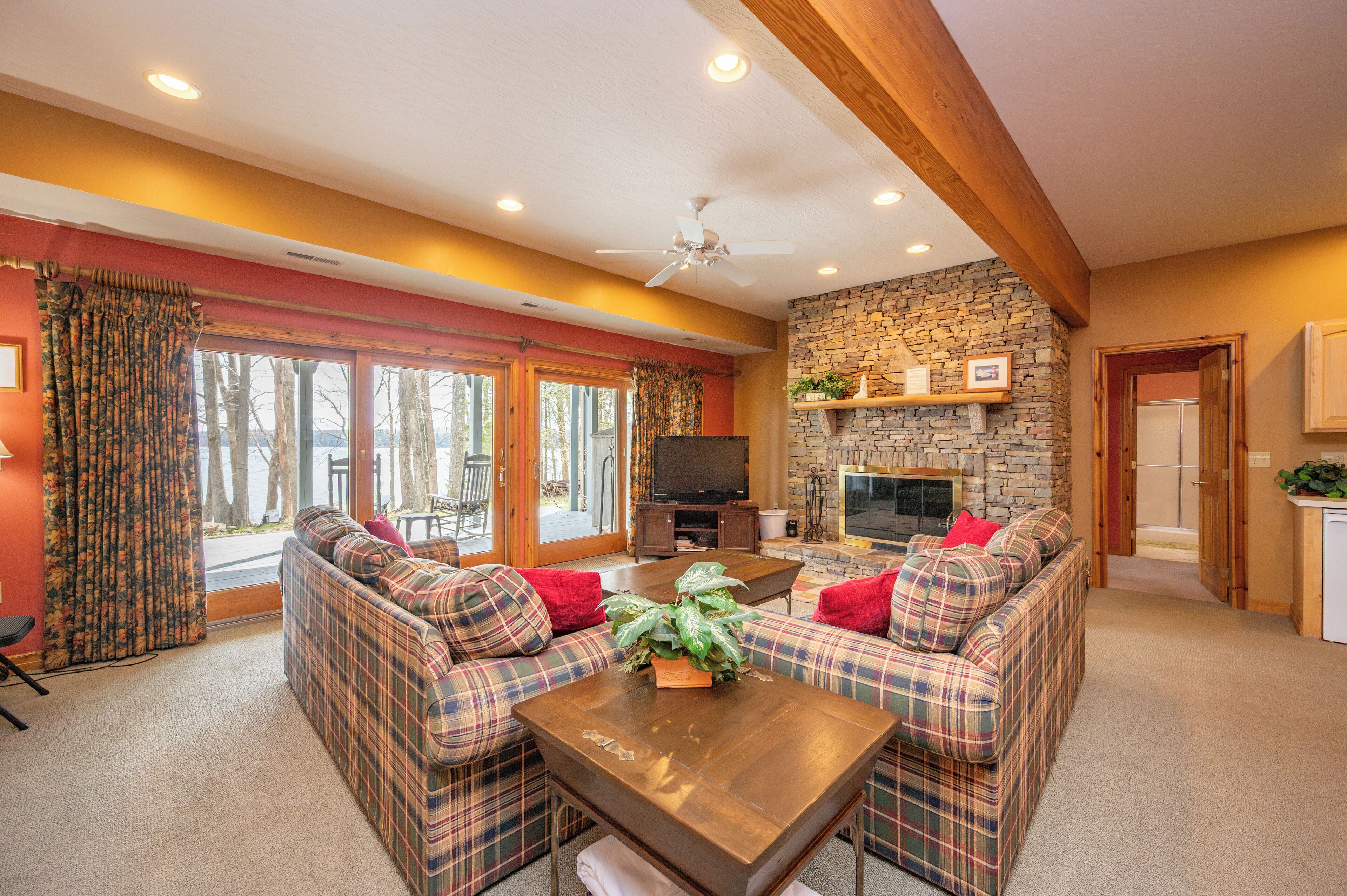 A cozy living room with plaid sofas, a wooden coffee table, a stone fireplace, and a television.