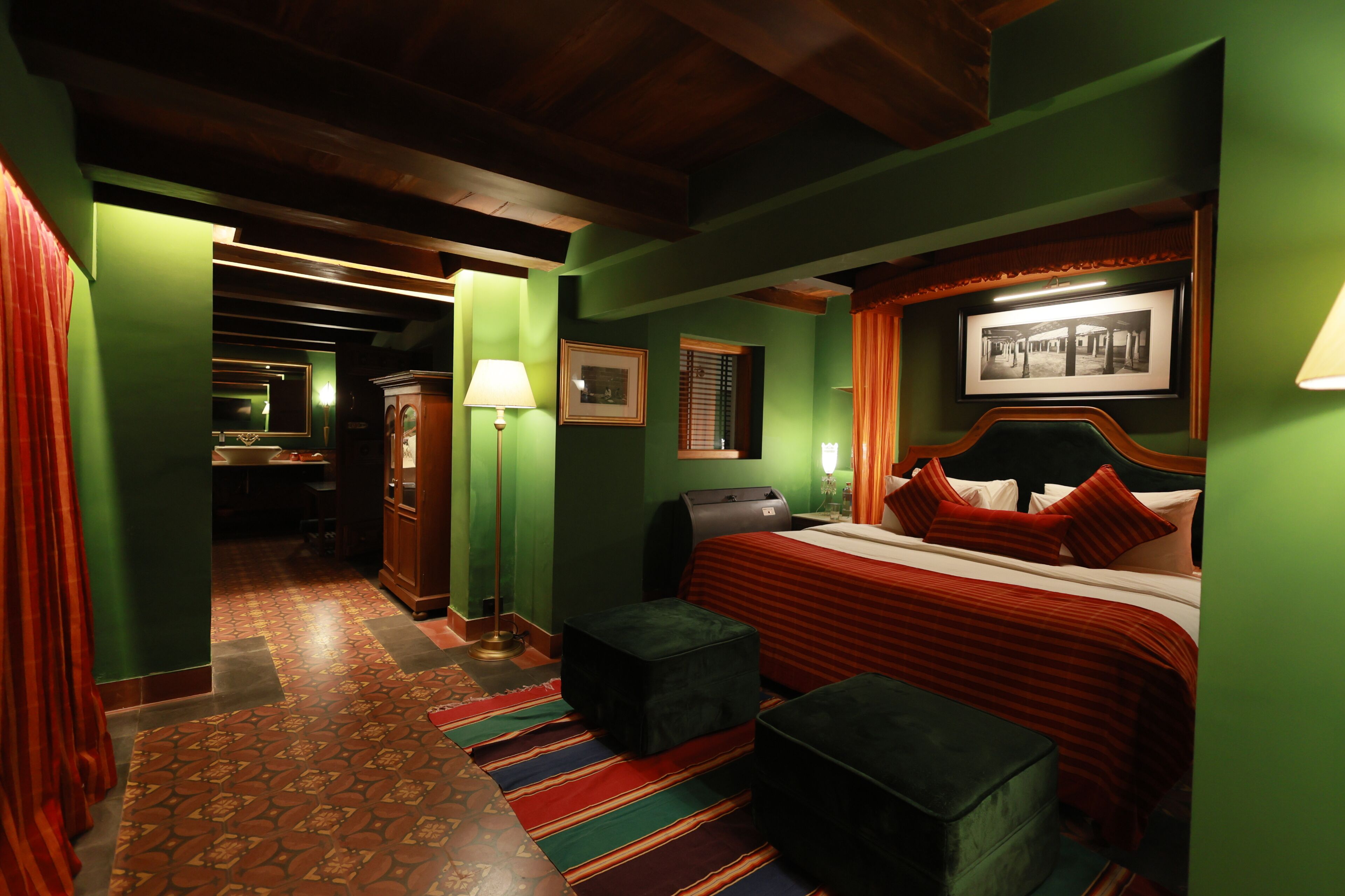 Habitación de hotel con cama, escritorio, lámpara, un cuadro en la pared y alfombra estampada.