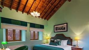 Una stanza con soffitto in legno, un letto con copripiumino verde e blu, una scrivania con sedia verde e un pavimento in legno a motivi.