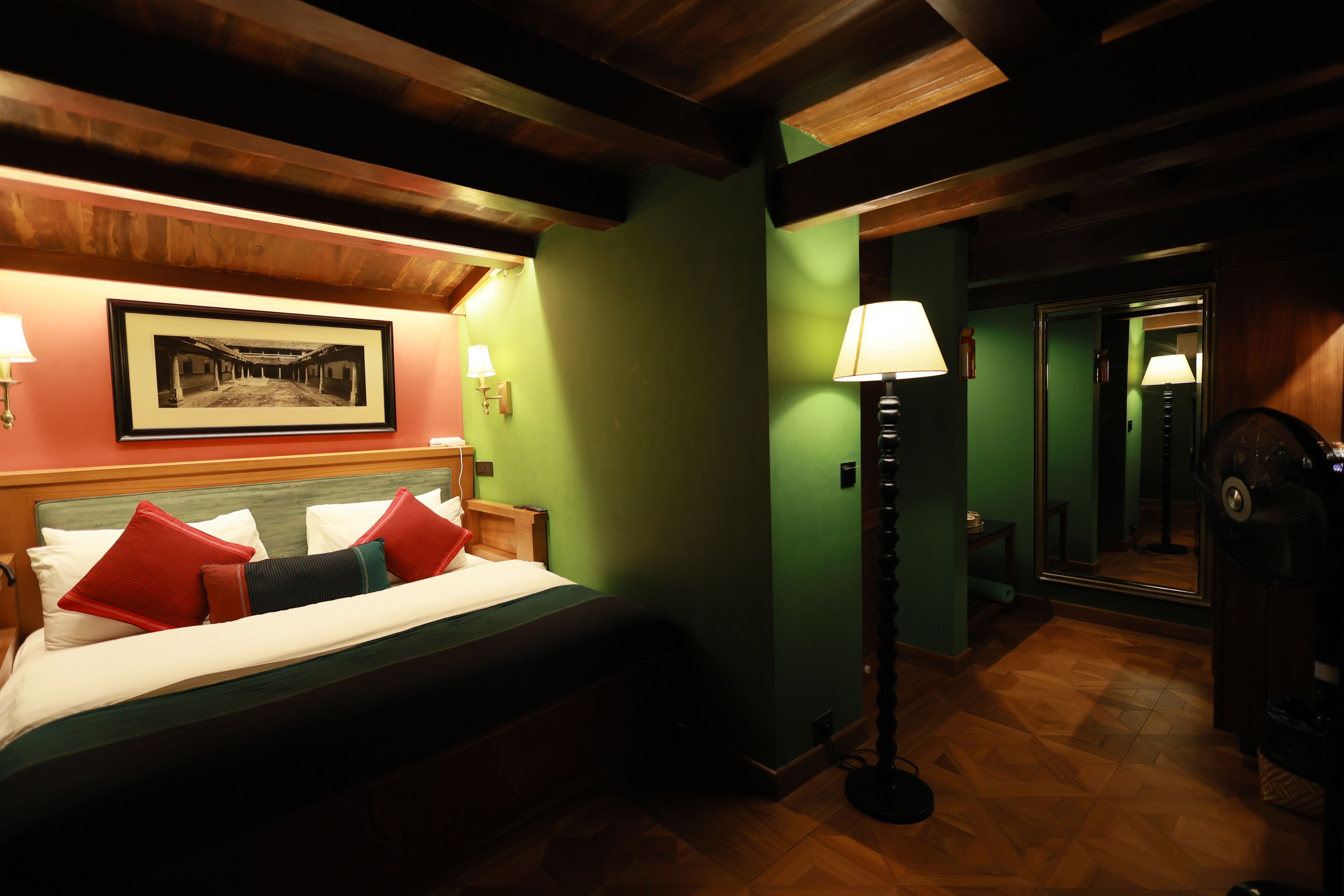 Une chambre d’hôtel avec un lit, une table de chevet, une lampe, un tableau encadré au mur et un miroir.