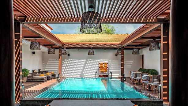 Area piscina con vista sul cielo attraverso una pergola in legno, zona relax con mobili in vimini e una piccola cascata.