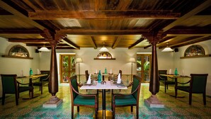 Zona pranzo con soffitto in legno, sedie imbottite verdi, un tavolo centrale e piastrelle del pavimento decorate.
