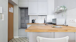 Een compacte keuken met witte kastjes, een houten aanrecht, een waterkoker, een magnetron en een kleine plant op een plank.