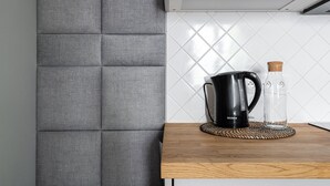 Een keuken met een grijze gestoffeerde scheidingswand, een zwarte koffiezetapparaat, een glazen karaf en een houten tafel.