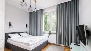Een moderne slaapkamer met een groot bed, grijze gordijnen, een televisie en een raam met een plant.
