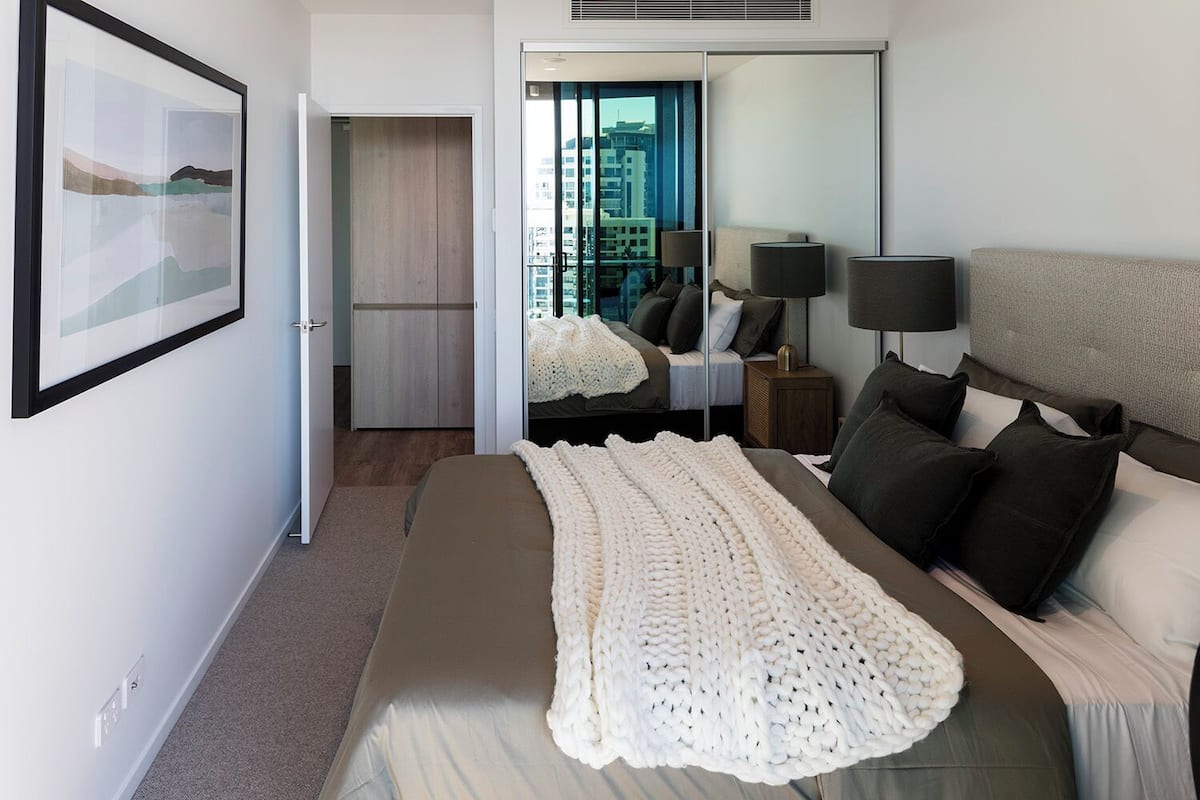 Habitación de hotel moderna con una cama grande, vistas de la ciudad a través de la ventana, un armario y un cuadro enmarcado en la pared.