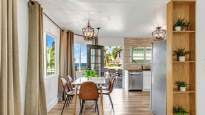 A modern kitchen with a built-in dishwasher, wooden shelving with potted plants, and a dining area with a table and chairs.