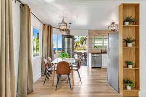 A modern kitchen with a built-in dishwasher, wooden shelving with potted plants, and a dining area with a table and chairs.