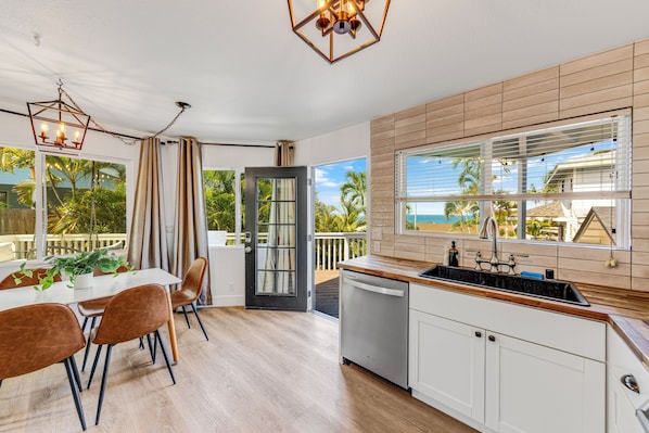 A modern kitchen with a wooden countertop, white cabinets, and a view of the ocean through large windows. - Royal Point Modern Hale (Kailua Kona)