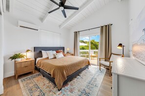 A bedroom with a bed, nightstands, a ceiling fan, a window with curtains, and a view of greenery outside.
