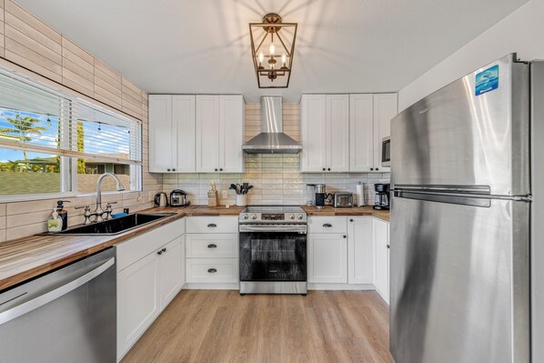A modern kitchen with white cabinets, stainless steel appliances, a wooden countertop, and a view of the outdoors.