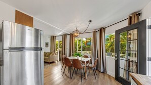A modern kitchen with a stainless steel refrigerator, a dining area with wooden chairs, and a view of the outdoors through large windows.