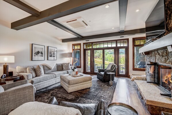 Relax in this inviting living room with a sofa set, ottoman, and armchair, surrounded by a large window and fireplace.