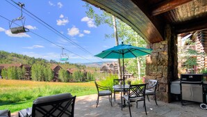 An outdoor patio with stone flooring, a table with chairs, a green umbrella, and a barbecue grill. - Remodeled 3br Condo In Bachelor Gulch - Ski In/out 3 Bedroom Condo (Avon)