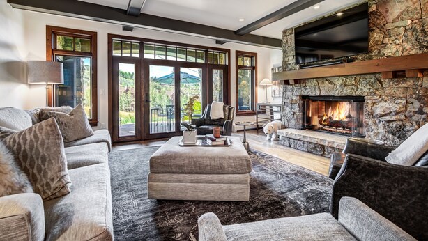 A spacious living room with a stone fireplace, comfortable seating, and large windows offering a view of the outdoors. - Remodeled 3br Condo In Bachelor Gulch - Ski In/out 3 Bedroom Condo (Avon)