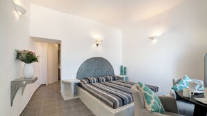 A modern bedroom with a bed, bedside tables, a chair, and a desk with a cup and saucer. - Remvi Suites (Santorini)