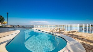 A swimming pool with a view of the sea, surrounded by a white fence and equipped with lounge chairs and tables. - Lagoon Tower 1301 3 Bedroom Condo (Gulf Shores)