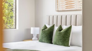 Un lit bien fait, agrémenté d’oreillers verts, d’une lampe de chevet blanche et d’une œuvre d’art encadrée au-dessus du lit.