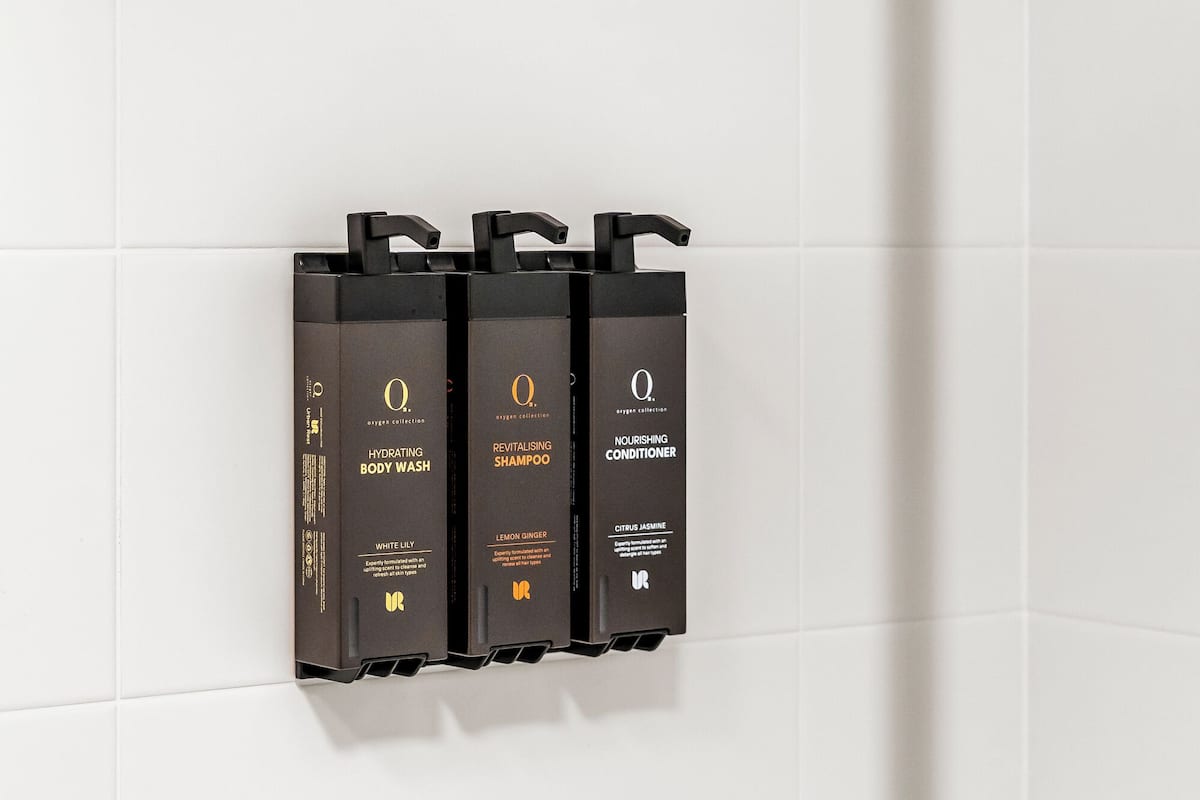 Un ensemble de distributeurs de produits de toilette noirs, fixés sur un mur recouvert de carreaux blancs.