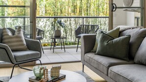 Un salon moderne avec un canapé gris, des fauteuils et une table basse. Il y a un balcon avec vue sur des bambous.