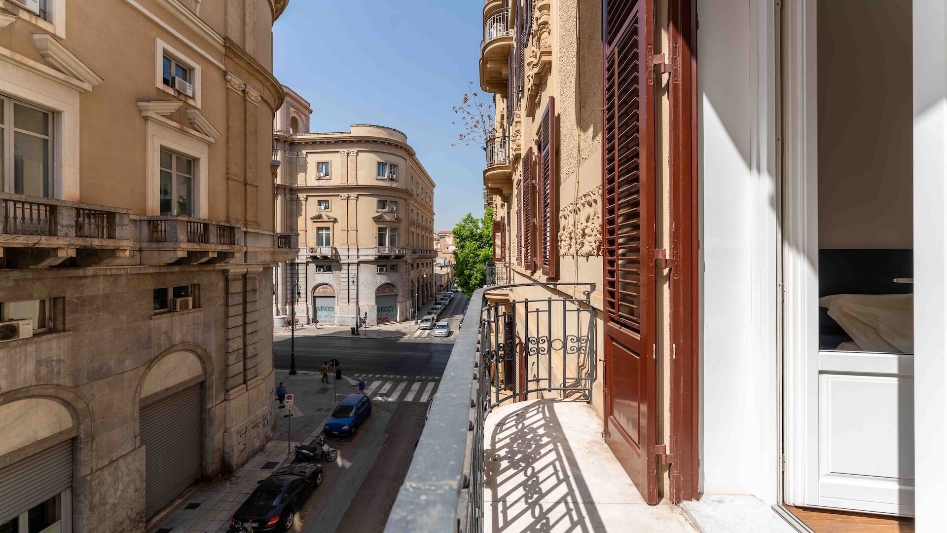 A narrow street with buildings on either side, a clear sky, and a few parked cars.