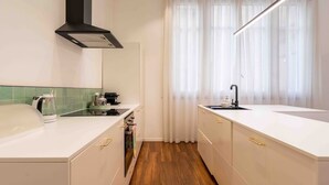 A modern kitchen with a stove, coffee maker, and a window with curtains.