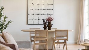Un coin repas avec une table blanche et quatre chaises en bois. Un grand tableau abstrait est accroché au mur, au-dessus de la table.