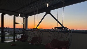 A rooftop terrace with hanging netted chairs and a view of the sunset.