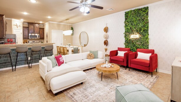 A modern living room with a white sofa, red armchairs, a coffee table, and a kitchen in the background.