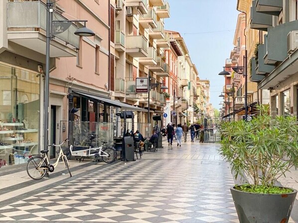A pedestrian street with a checkered floor, buildings with balconies, and a potted plant on the right.